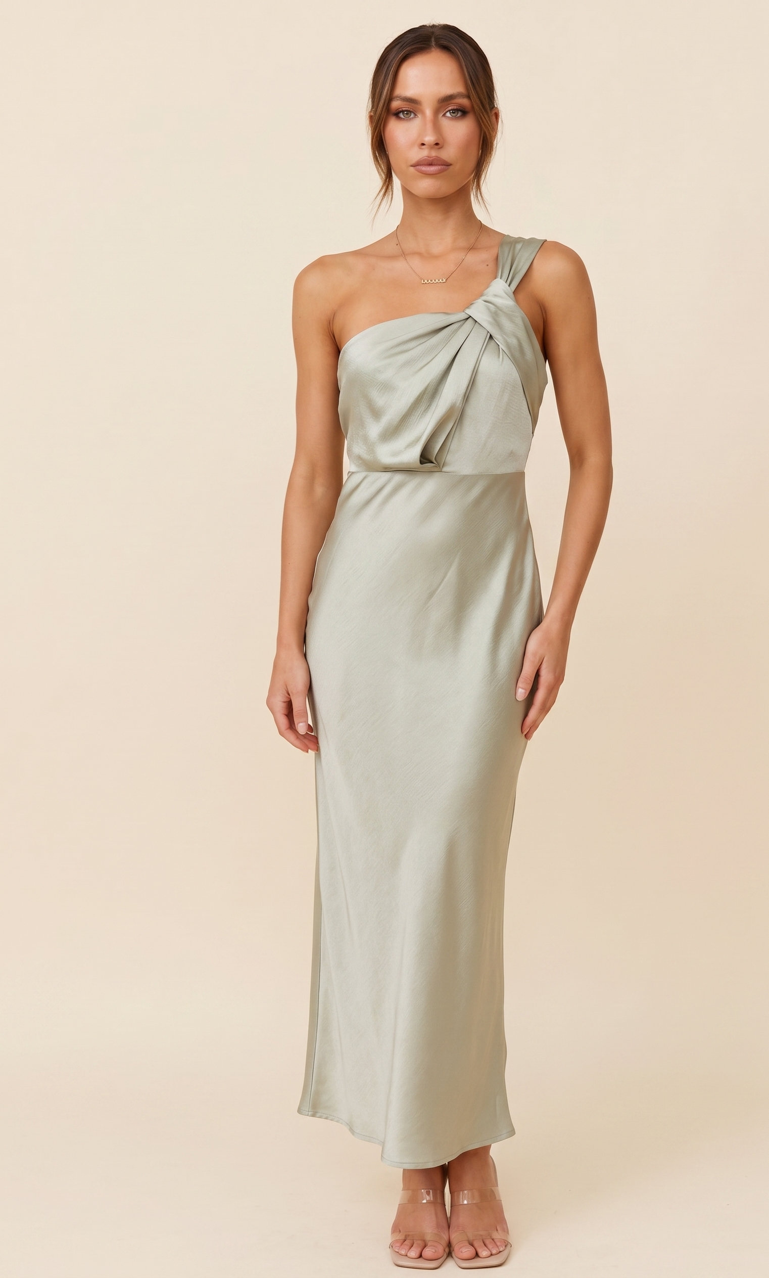Woman wearing a light green one-shoulder dress against a beige background
